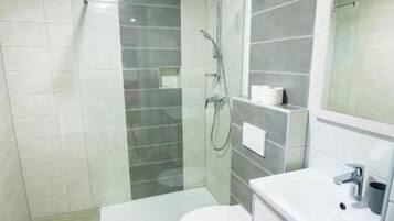 Een moderne badkamer met een douchecabine van glas, een toilet en een wastafel met spiegel.