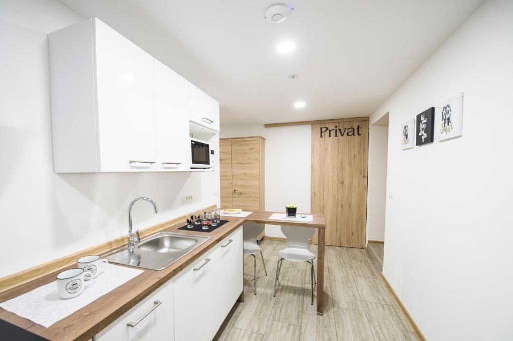 Una cocina moderna con armarios blancos, encimera de madera, un lavamanos y un comedor con dos sillas.