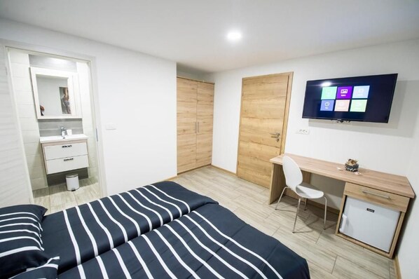 A bedroom with a bed, a desk, a chair, a TV, and a wardrobe.
