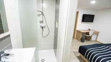 Ein Hotelzimmer mit Dusche, Schreibtisch, Bett und Fernseher.