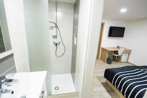 Una habitación de hotel con ducha, escritorio, cama y televisión.