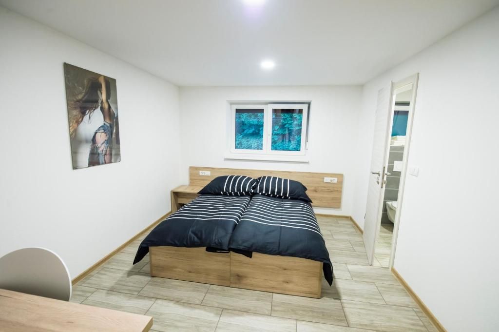 A bedroom with a bed, a window, a door, and a painting on the wall.