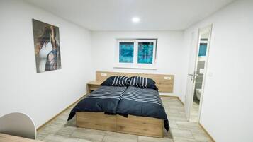 A bedroom with a bed, a window, a door, and a painting on the wall.