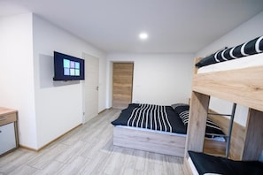 Une chambre avec un lit superposé, un bureau, un téléviseur fixé au mur et une porte en bois.