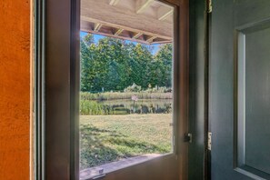 A view through a door with a wooden frame, leading to a grassy area with a pond and trees. - Kettlebrook Ski-In/Ski-Out Condo with Fireplace (Ludlow)