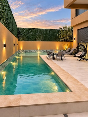 Un espace piscine extérieur moderne, doté d’un coin salon et d’un mur décoratif.