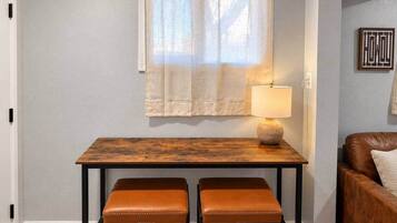 Un petit coin repas avec une table et deux chaises, une lampe sur la table et un canapé à l’arrière-plan.