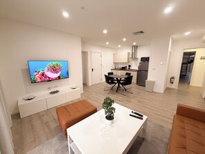 A modern living room with a flat-screen TV, a dining table with chairs, a kitchen area with a refrigerator, and a staircase leading to another level. - Ocean View 1-Bed Apt Downtown CasaAmarilla305 (Oranjestad)
