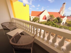 A balcony with wicker chairs and a table, overlooking a building with a red roof and a tower. - Ocean View 1-Bed Apt Downtown CasaAmarilla305 (Oranjestad)