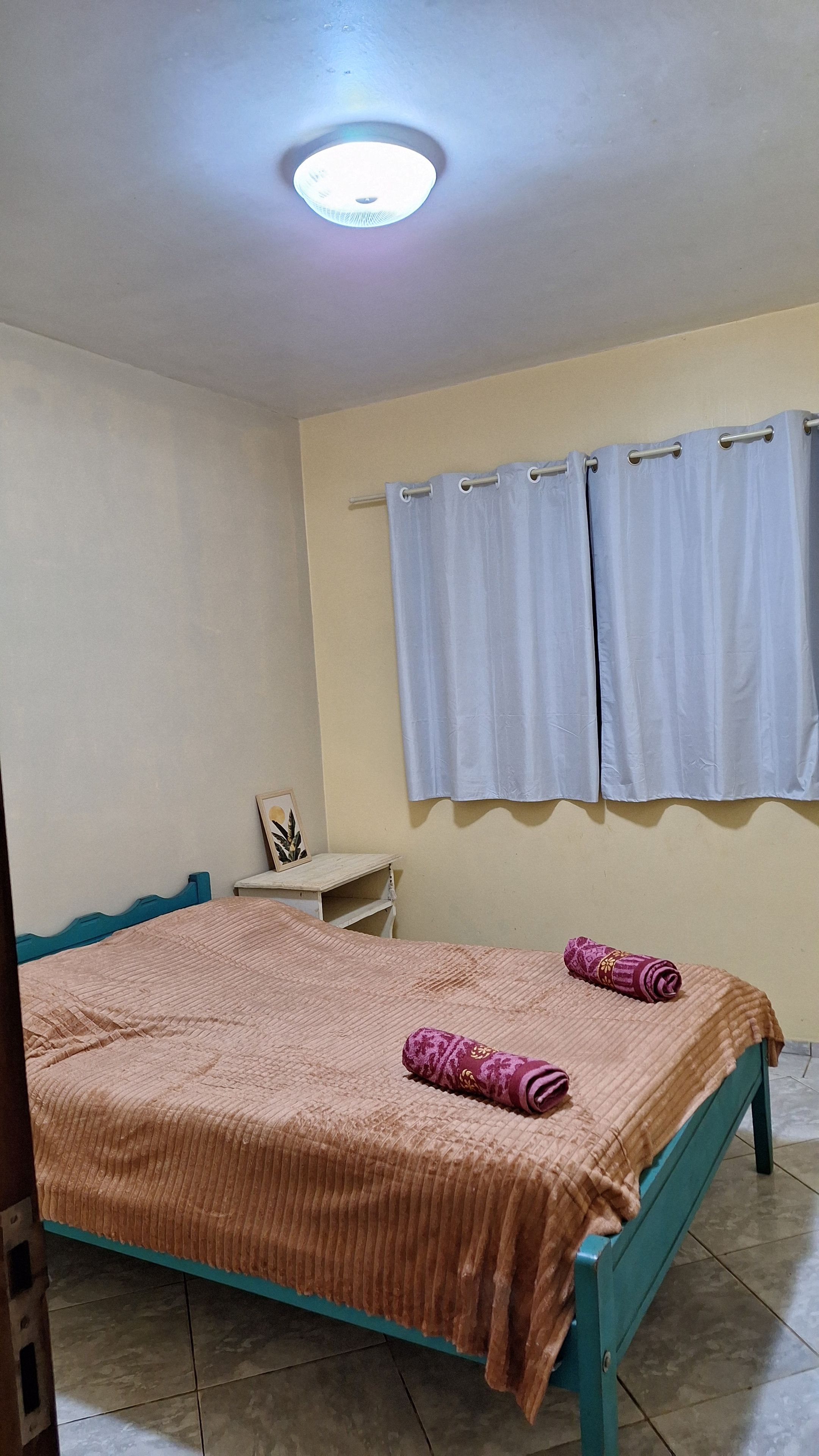 Une chambre à coucher avec un lit, des rideaux, une table de chevet et un luminaire au plafond.