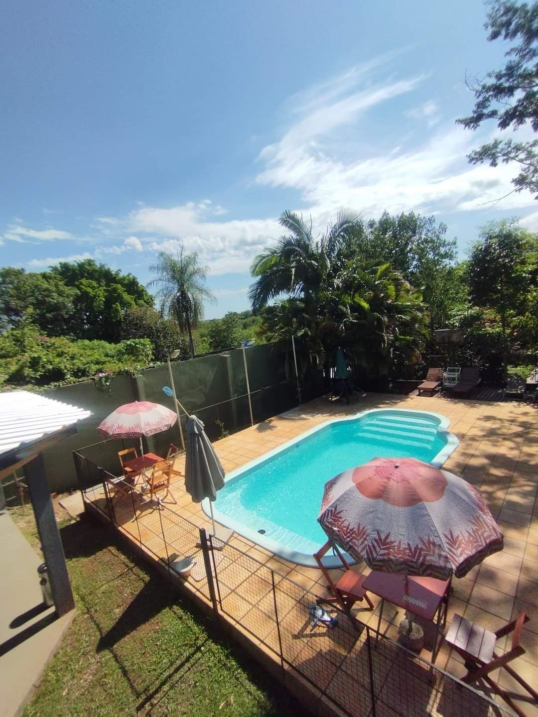 Un jardin avec une piscine, entouré d’une clôture, et aménagé avec du mobilier d’extérieur et des parasols.