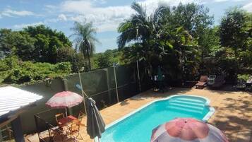 Un jardin avec une piscine, entouré d’une clôture, et aménagé avec du mobilier d’extérieur et des parasols.