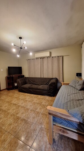 A living room with a brown sofa, a television, a ceiling fan, and an air conditioning unit. - kuri hospedaje (Puerto Iguazú)