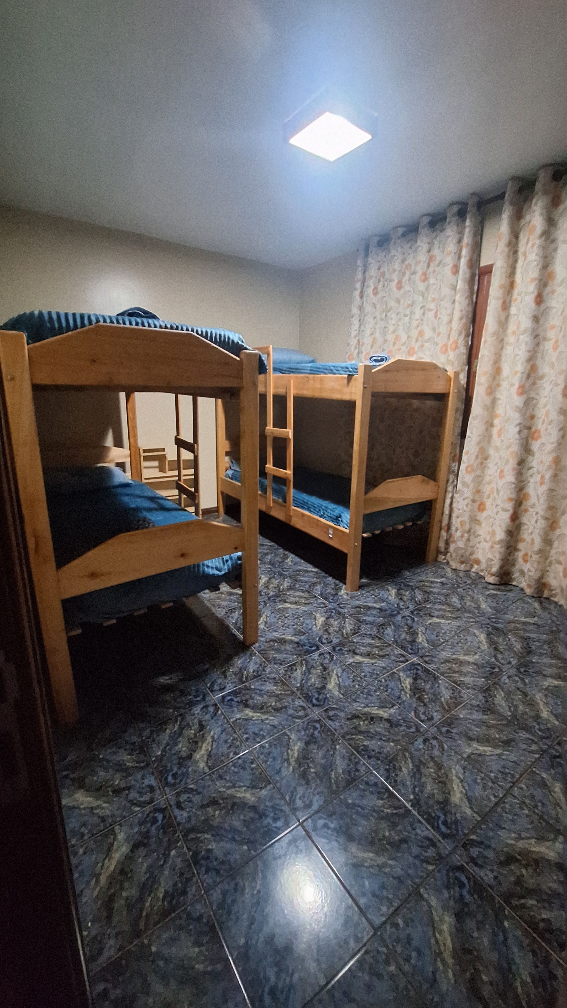 A room with three wooden bunk beds, a tiled floor, and a ceiling light.