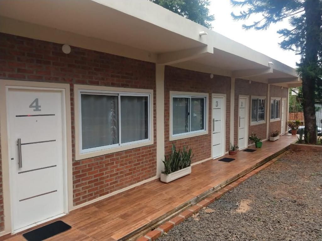 A row of numbered hotel rooms with a brick facade, large windows, and a covered outdoor area with potted plants.