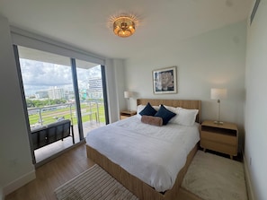 A modern bedroom with a large bed, two bedside tables, a chandelier, and a city view through large windows. - New 2 bedroom condo in the middle of bustling Midtown/Wynwood & Design District (Miami)