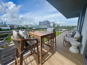 A balcony with a wooden table and chairs, a view of the cityscape, and a railing. - New 2 bedroom condo in the middle of bustling Midtown/Wynwood & Design District (Miami)