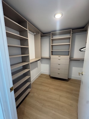 Ein begehbarer Kleiderschrank mit offenen Regalen, einer eingebauten Schubladenkommode und einer Deckenleuchte.
