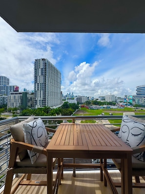 A balcony with a wooden table and chairs, overlooking a cityscape with high-rise buildings and a clear sky. - New 2 bedroom condo in the middle of bustling Midtown/Wynwood & Design District (Miami)