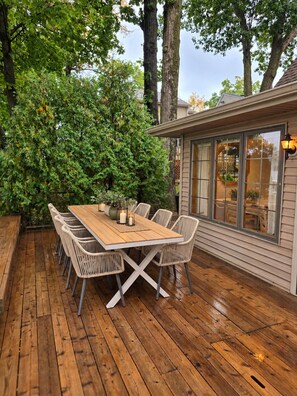Eine Holzterrasse im Freien mit einem Esstisch und Stühlen, umgeben von Bäumen.