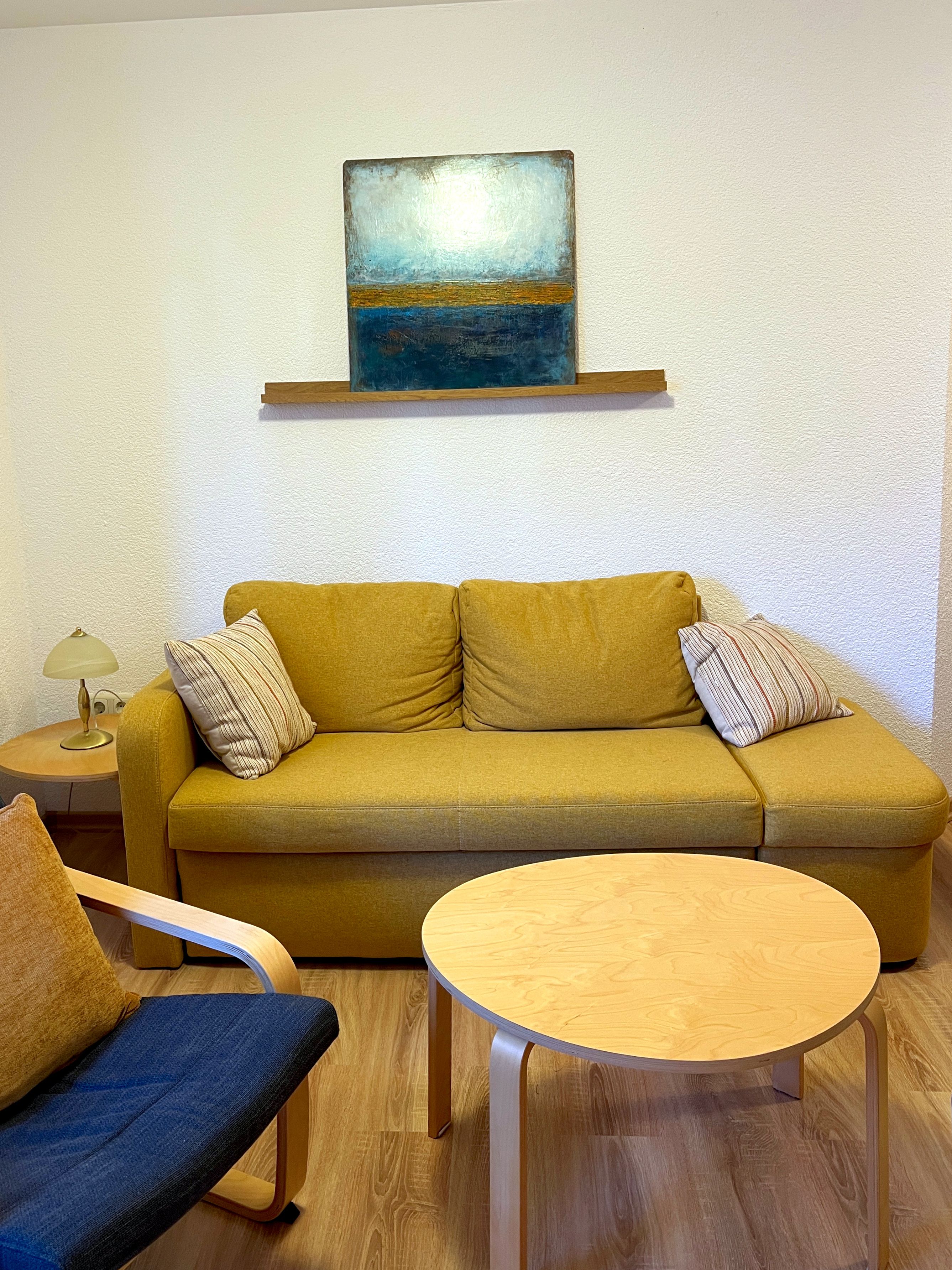 Ein Zimmer mit einer Couch, einem runden Holztisch, einer Lampe und einem Bild an der Wand.