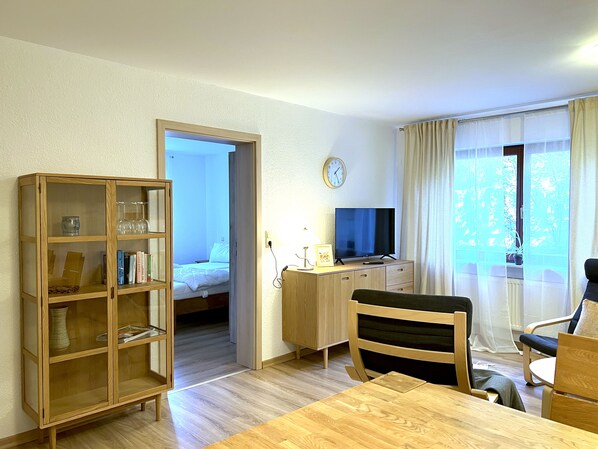 Una camera d'albergo con un armadio in legno, un letto, una scrivania con televisore, una sedia e una finestra con tende.