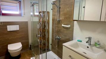 Une salle de bain moderne avec une douche à parois de verre, des toilettes, un lavabo avec un miroir au-dessus et un revêtement de sol en bois.