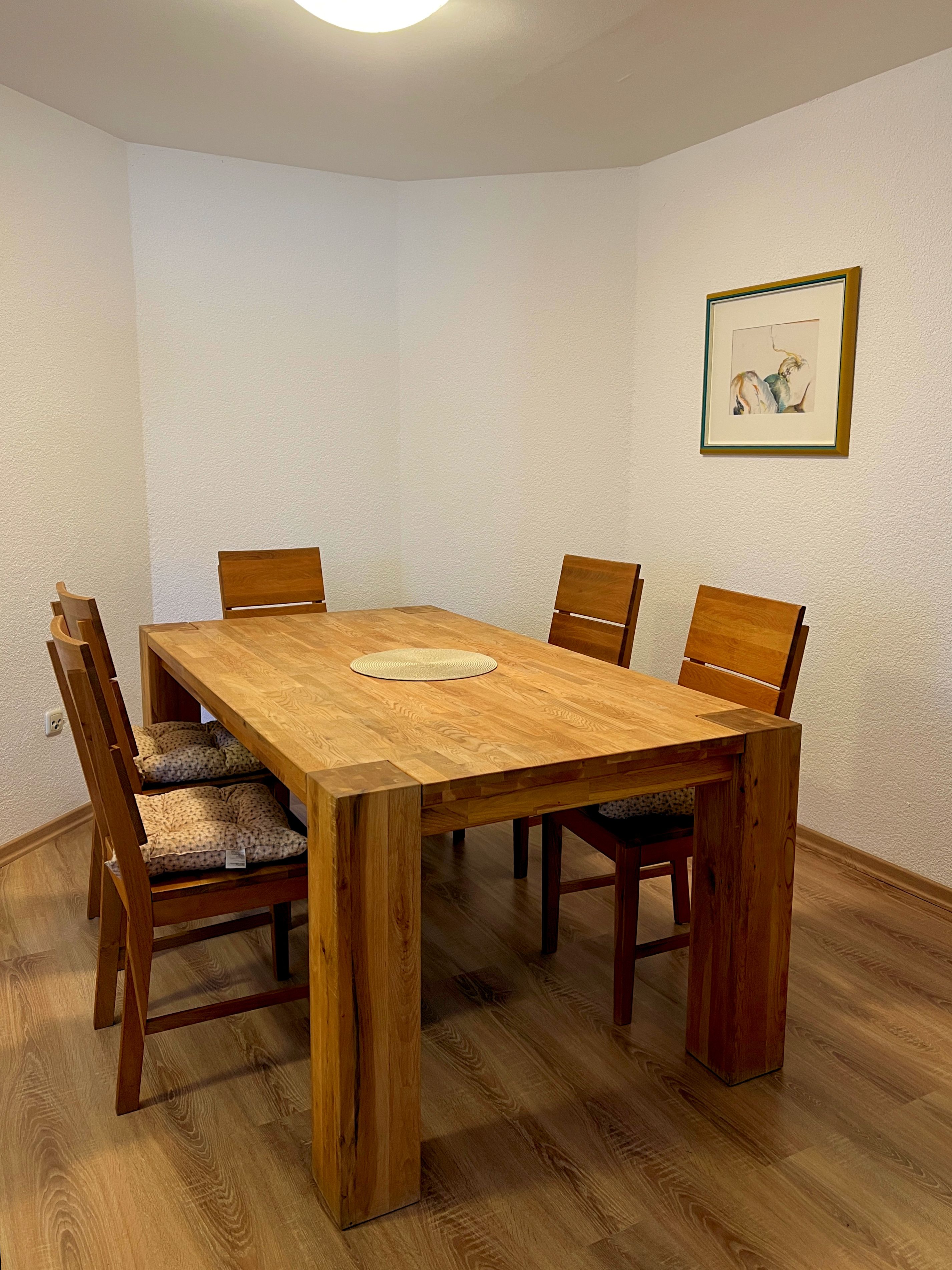 Un comedor con una mesa y sillas de madera, un cuadro en la pared y un interruptor de luz.
