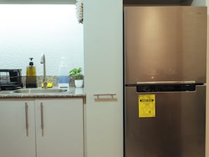 Ein Edelstahl-Kühlschrank mit einem Digital Inverter-Etikett, ein Spülbecken, ein Seifenspender, ein Schwamm und ein Topfpflanze auf der Arbeitsplatte.