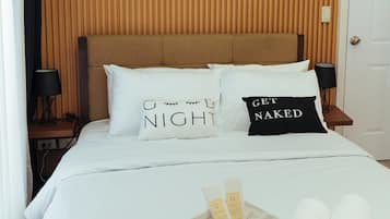Ein ordentlich bezogenes Bett mit weißer Bettwäsche, zwei Kissen mit Aufdruck, ein Nachttisch mit Lampe und eine Wand mit drei gerahmten Bildern.