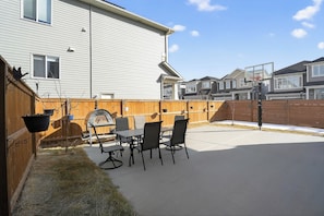 Ein Hinterhof mit einer Terrasse, einem Grill, einem Esstisch und Stühlen.