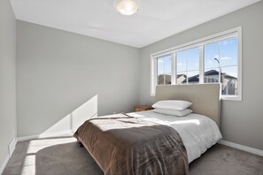 Ein Schlafzimmer mit einem Bett, einem Nachttisch, einem Fenster und einer Deckenleuchte.