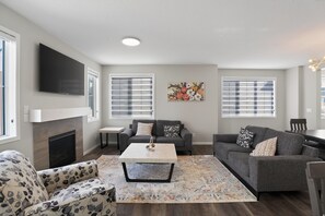 A living room with a fireplace, a flat-screen TV, two sofas, a coffee table, and a rug. - Spacious 3BR Home | Parking | Near Airport & Shops (Calgary)