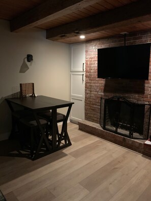 Una habitación con una mesa y sillas de madera, una chimenea de ladrillo y un televisor montado.