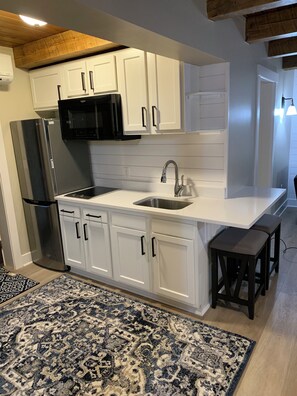 A modern kitchen with white cabinetry, a stainless steel sink, a black microwave, and a built-in refrigerator. - A Cozy suite near Seven Springs Mountain Resort  (Champion)
