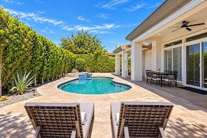 A swimming pool with a curved edge, surrounded by a patio area with chairs and a table. - Desert Dreamin' with Private Pool & Spa (Palm Desert)