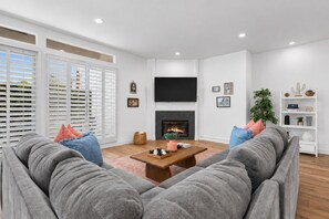 A modern living room with a fireplace, a flat-screen TV, and a large sectional sofa. - Desert Dreamin' with Private Pool & Spa (Palm Desert)