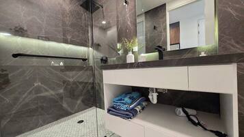 A modern bathroom with a glass shower enclosure, a vanity with a marble countertop, and a mirror above the sink.