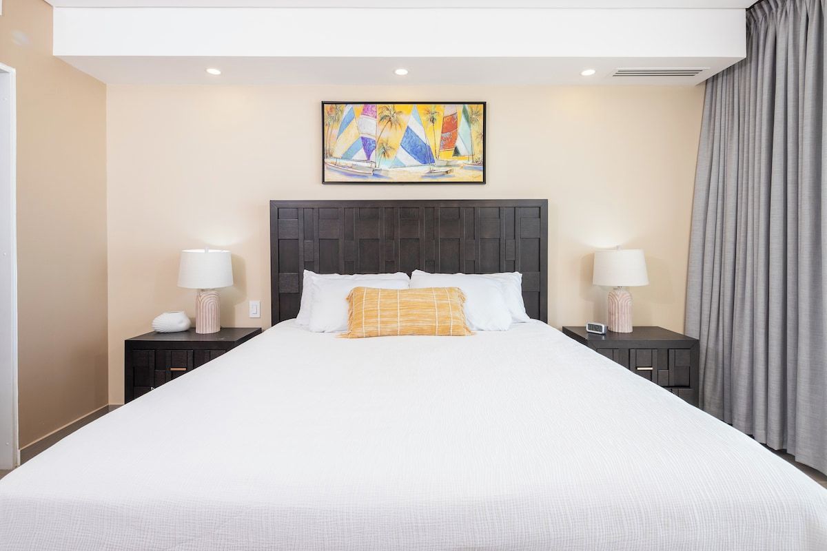 Une chambre d’hôtel avec un grand lit, deux tables de chevet, une tête de lit et un tableau au-dessus du lit.