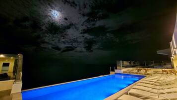 Una piscina con vista despejada al agua, un área de descanso con sillas y un edificio con fachada de vidrio.