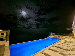 Une piscine offrant une vue dégagée sur l’eau, un espace détente avec des fauteuils et un bâtiment doté d’une façade en verre.