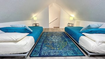 A room with two beds, a blue rug, and a staircase leading to an upper level.