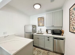A compact kitchen with a refrigerator, microwave, and dishwasher. - Cottage 7 Blue, Pet-Friendly One-Bedroom Cottage with Loft, Hot Tub (Wimberley)