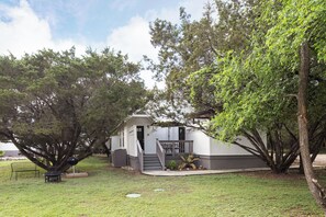A house with a covered porch, a barbecue grill, and a small patio area. - Cottage 8 Black, Pet-Friendly One-Bedroom Cottage with Loft, Hot Tub (Wimberley)