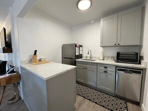 A compact kitchen with a refrigerator, microwave, and dishwasher. - Cottage 8 Black, Pet-Friendly One-Bedroom Cottage with Loft, Hot Tub (Wimberley)