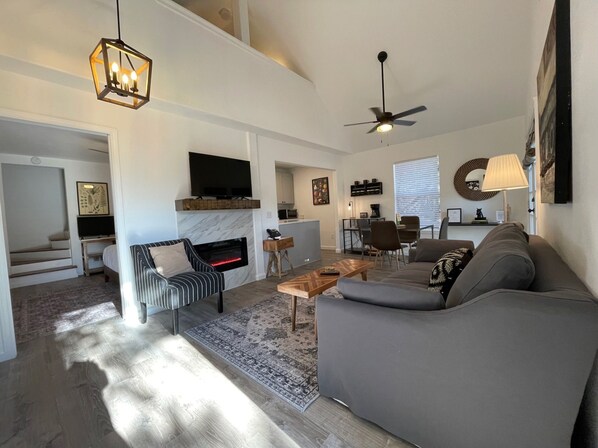 A modern living room with a fireplace, a sofa, a coffee table, and a television. - Cottage 8 Black, Pet-Friendly One-Bedroom Cottage with Loft, Hot Tub (Wimberley)