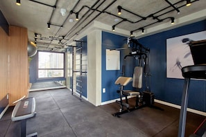 Een fitnessruimte met trainingsapparatuur, een loopband en een raam met uitzicht op gebouwen.