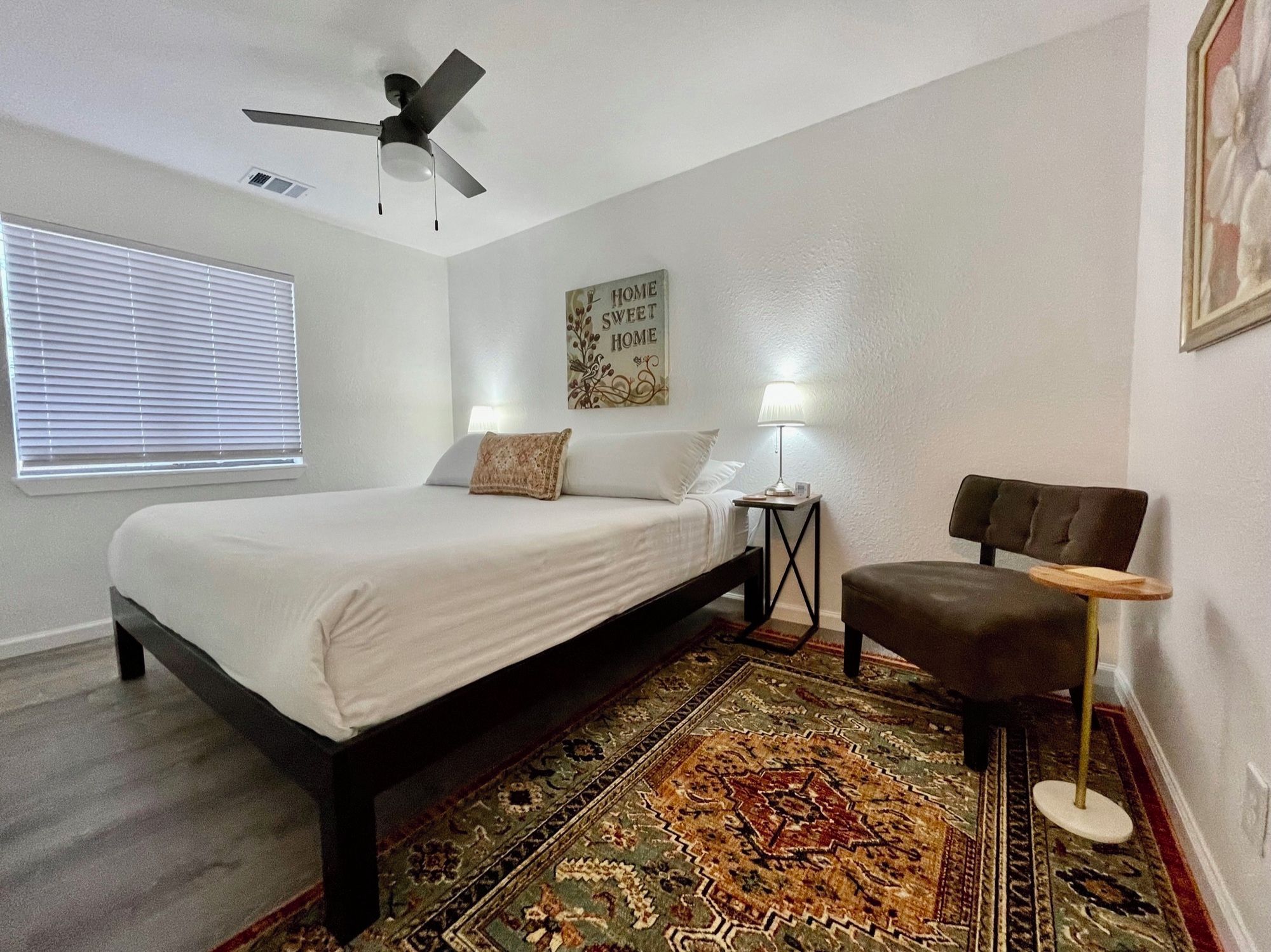 Une chambre à coucher comprenant un lit, un ventilateur de plafond, une table de chevet avec une lampe, une chaise et un tapis.
