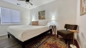 Une chambre à coucher comprenant un lit, un ventilateur de plafond, une table de chevet avec une lampe, une chaise et un tapis.