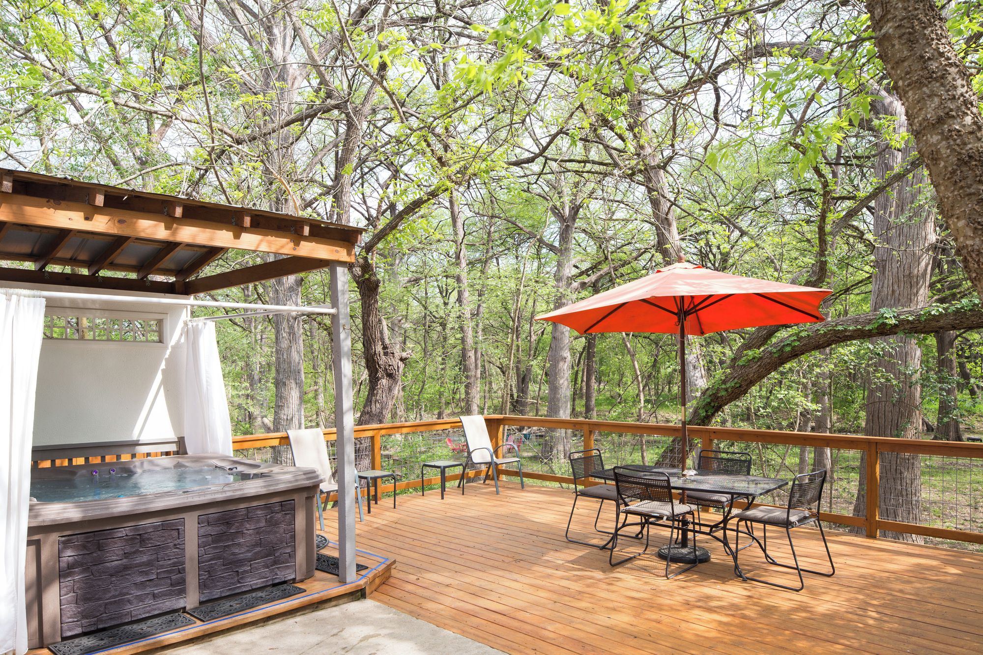 A wooden deck with a hot tub, outdoor seating, and a red umbrella.